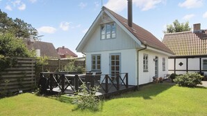 Ett vitt hus med ett sadeltak och en skorsten, omgivet av ett trädäck och en gräsplätt.