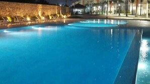Ein Schwimmbad bei Nacht mit umliegenden Gebäuden und einer Steinmauer.