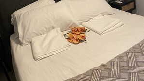 Ein ordentlich bezogenes Bett mit weißen Leinen, ein gerahmtes Bild an der Wand und eine Nachttischlampe.