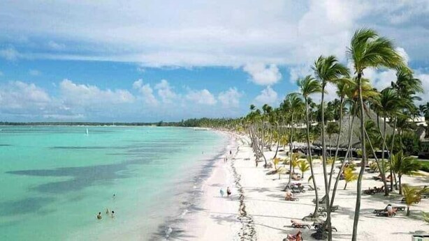 Ein Strand mit weißem Sand, türkisblauem Wasser und Palmen.