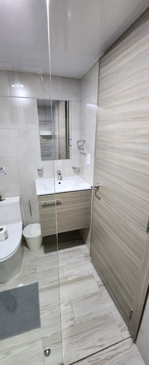 A modern bathroom with a glass partition, a sink, a toilet, and a mirror. - Brand New Punta Cana 2 Bedroom 2 B Condo (Punta Cana)