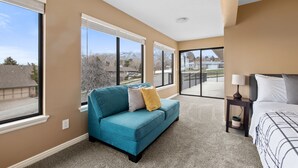A bedroom with a large window, a blue sofa, and a bed with a nightstand.