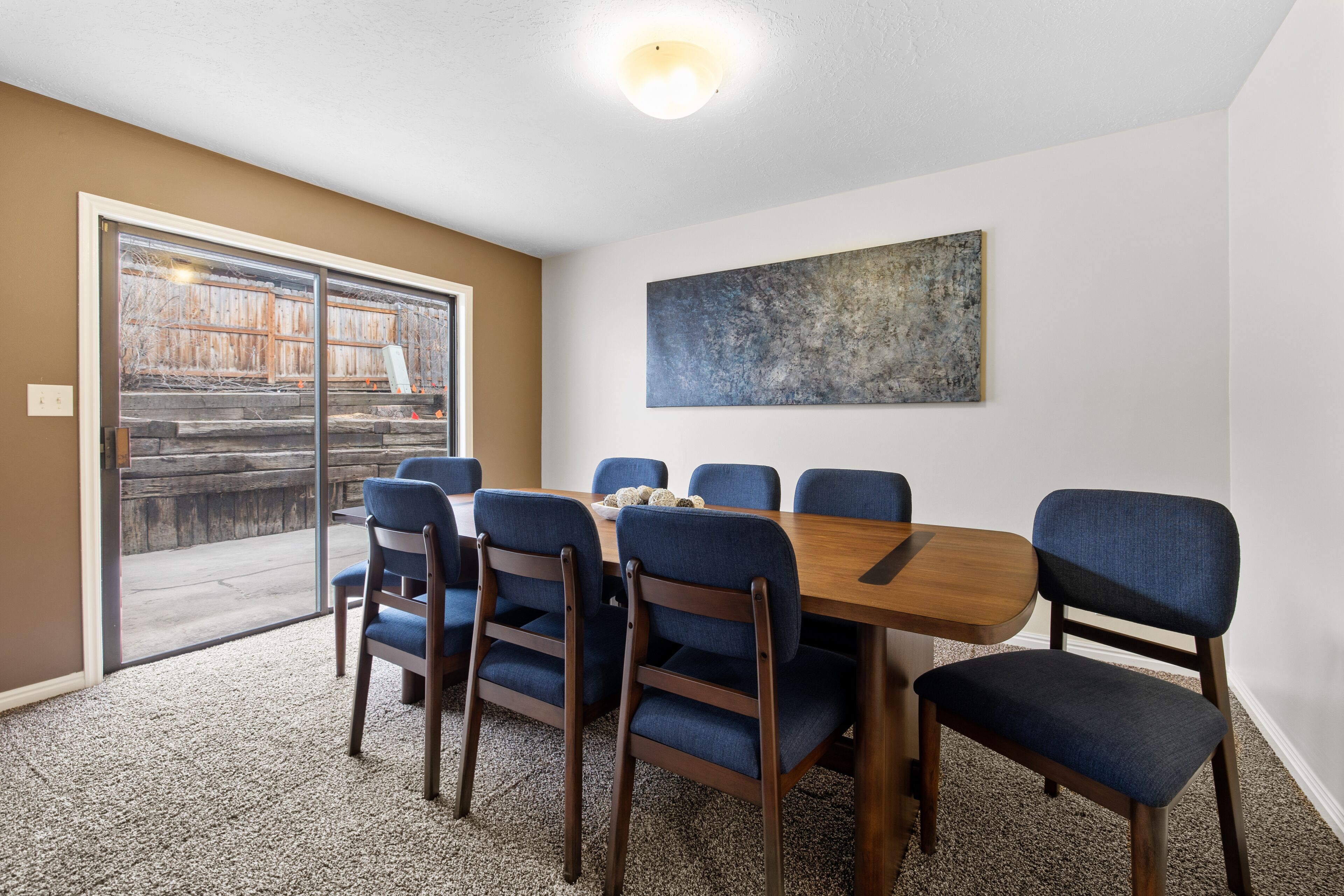 Un salón de conferencias con una mesa de madera y sillas tapizadas en azul, un cuadro abstracto grande en la pared y una puerta de cristal corredera que da a un espacio exterior.