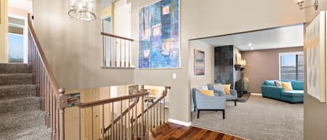 A spacious living area with a wooden staircase, a large abstract painting, and a cozy seating area with a blue sofa.