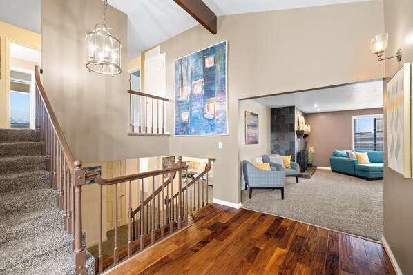 A spacious living area with a wooden staircase, a large abstract painting, and a cozy seating area with a blue sofa.
