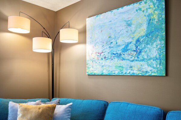 A living room with a blue sofa, three floor lamps, and a large abstract painting on the wall.