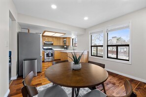Una cocina moderna con armarios de madera, un refrigerador de acero inoxidable y una zona de comedor con una mesa y sillas de madera.
