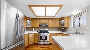 A modern kitchen with wooden cabinets, a stainless steel refrigerator, an oven, and a large island with a sink.