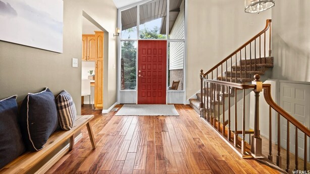 A wooden-floored entrance with a red door, a bench with cushions, and a staircase with a wooden railing.