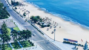 Eine Küstenstraße mit Strand, Palmen und einer Statue.
