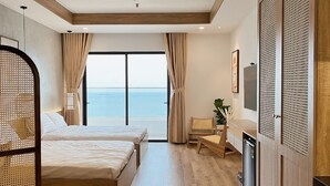 Ein Hotelzimmer mit zwei Betten, einem Schreibtisch, einem Stuhl, einem Fernseher und Blick auf das Meer.