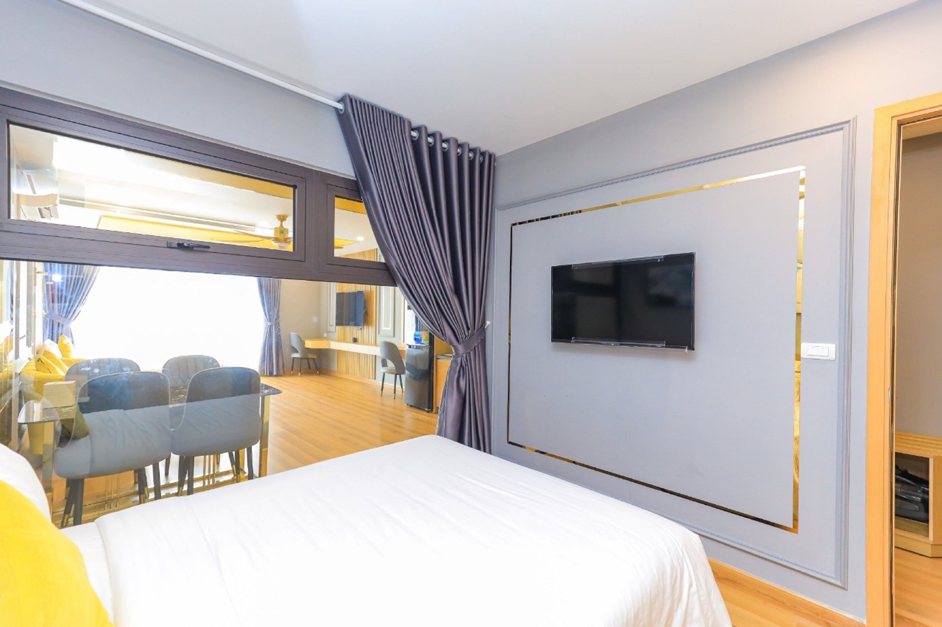 Hotellihuone, jossa on sänky, seinälle asennettu televisio, työpöytä tuoleineen ja suuri ikkuna, jossa on verhot.