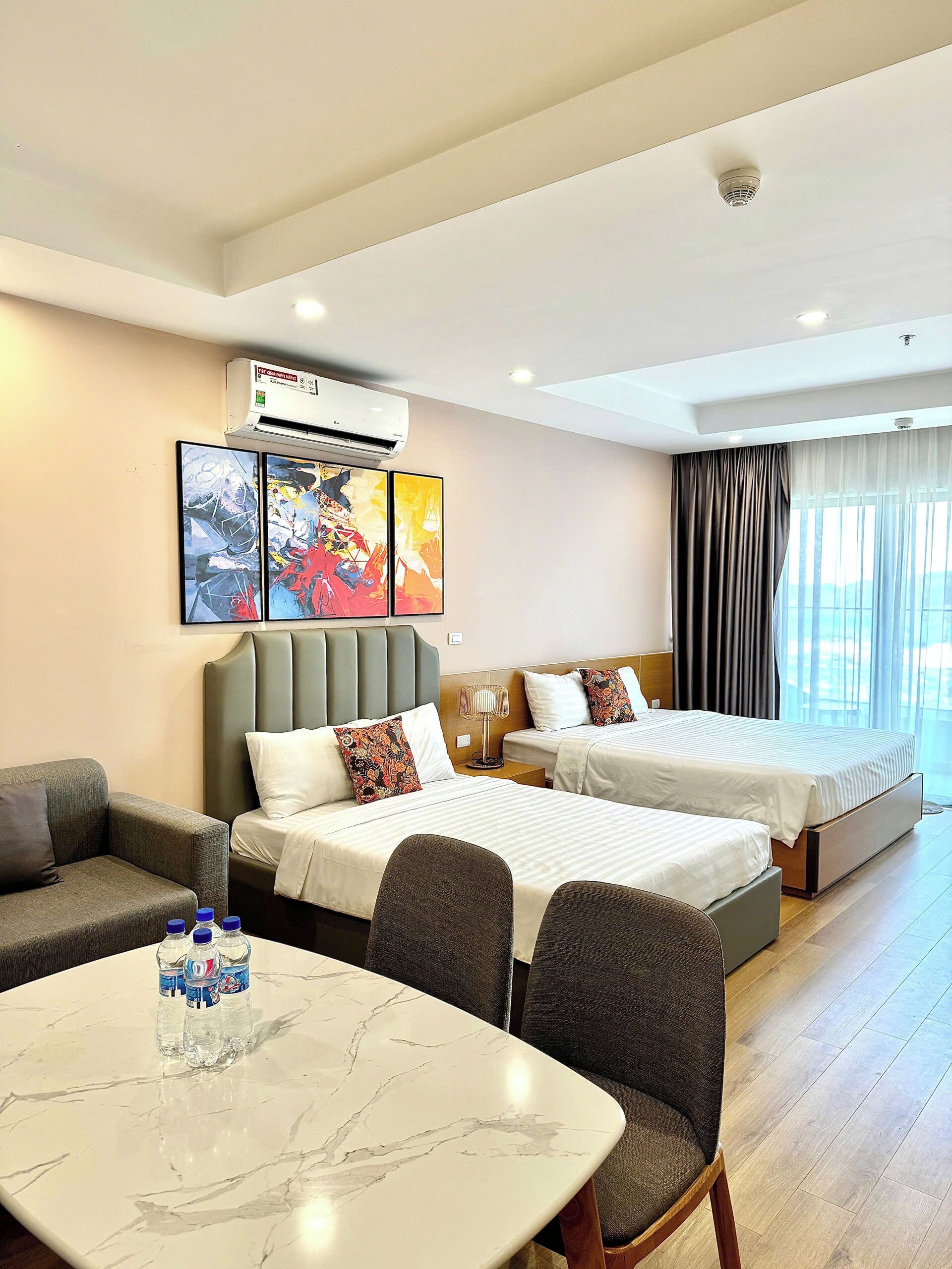 A hotel room with two beds, a sofa, a marble table, and artwork on the wall.