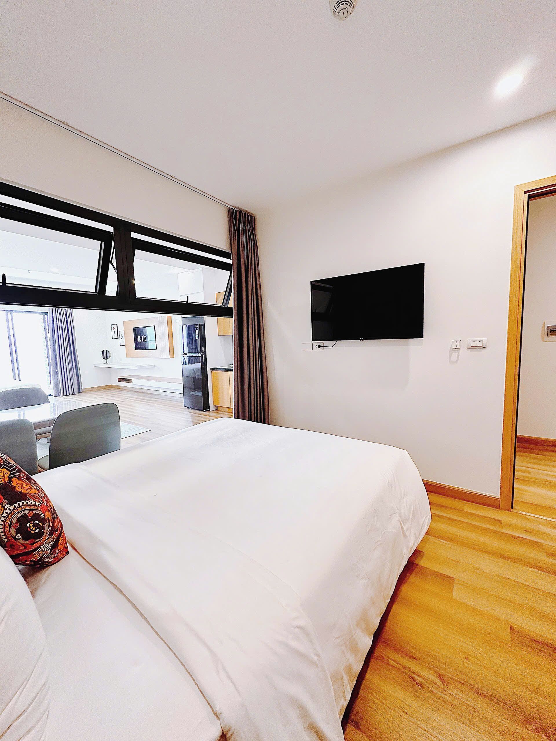 Habitación de hotel con una cama grande, un televisor de pantalla plana montado en la pared y vistas al exterior a través de un ventanal.