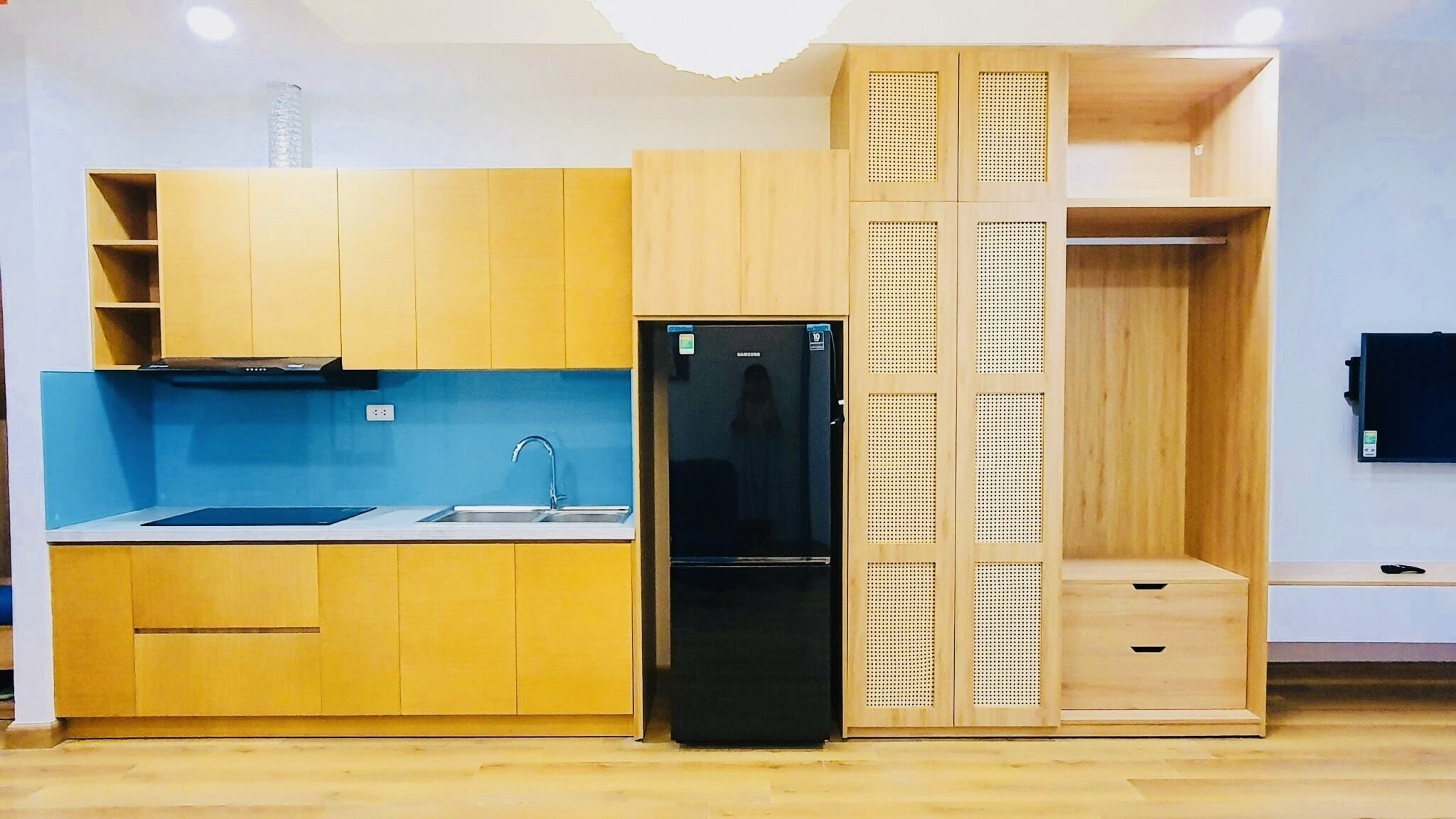 A compact kitchen with wooden cabinets, a black refrigerator, and a blue backsplash.