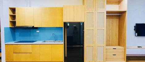 A compact kitchen with wooden cabinets, a black refrigerator, and a blue backsplash.