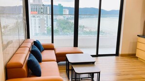 Ein modernes Wohnzimmer mit einer Couch, einem kleinen Tisch und Blick auf Stadt und Wasser durch große Fenster.