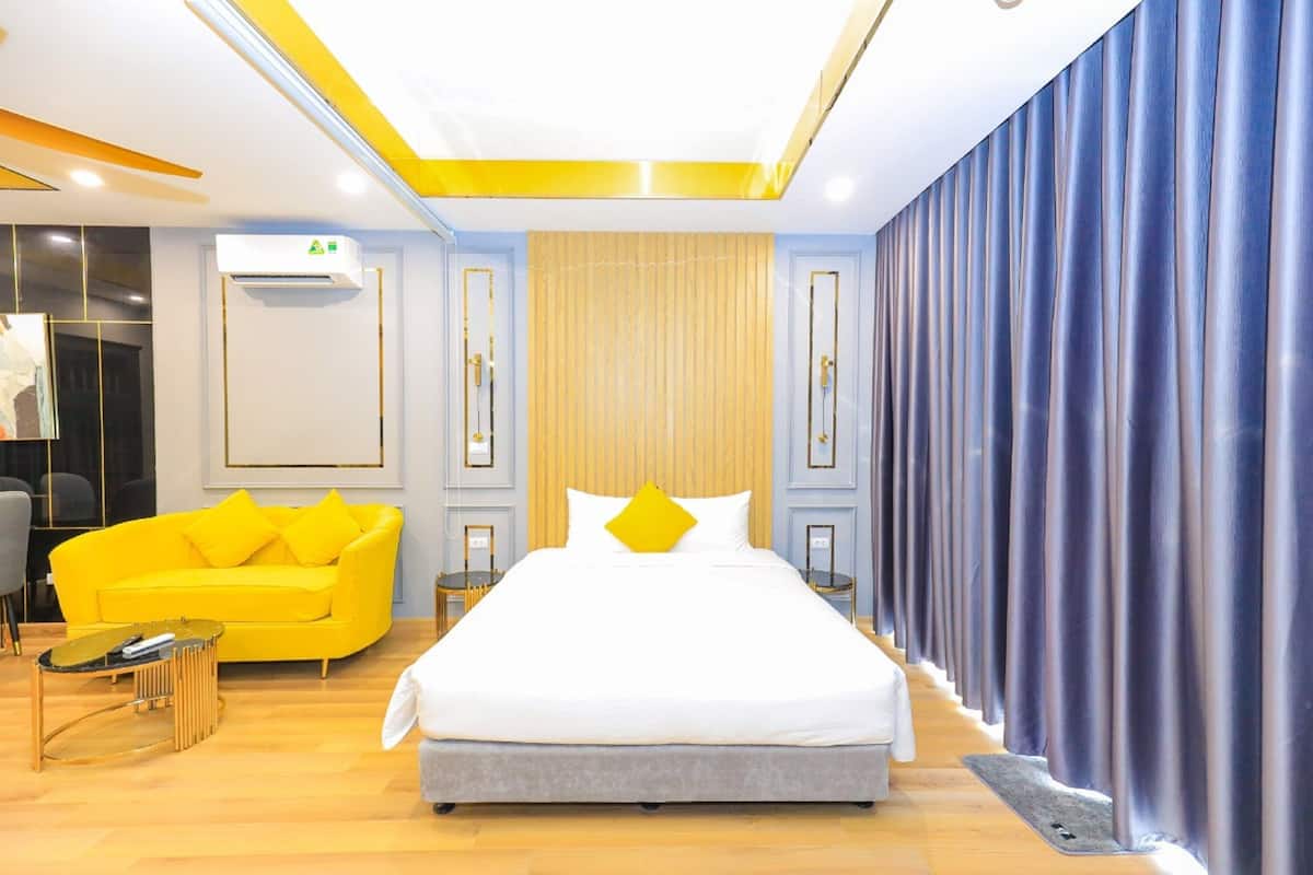 A modern hotel room with a large bed, a yellow sofa, and a wooden floor.