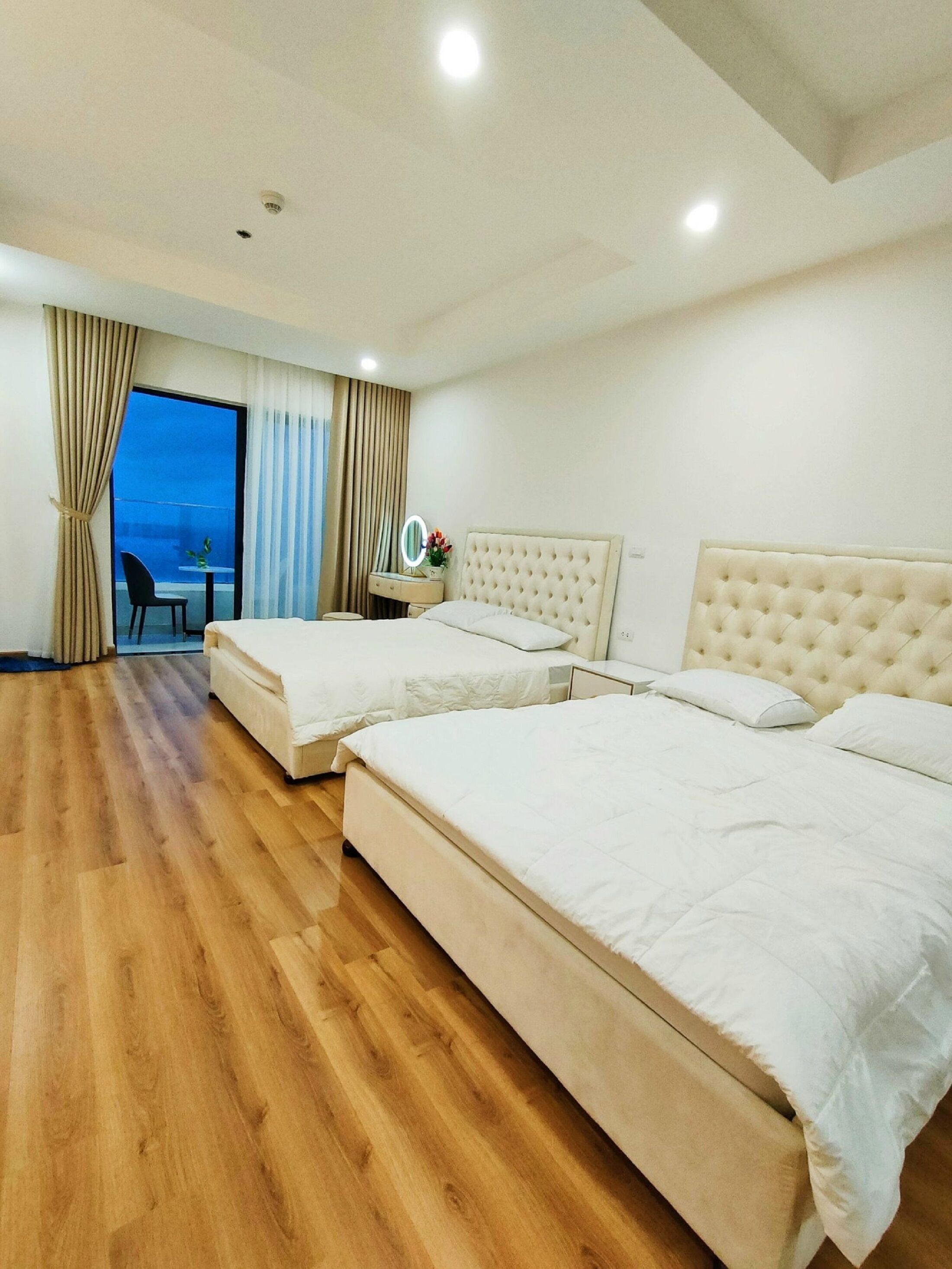Habitación de hotel con dos camas, una mesita con una silla, un espejo y vistas al exterior.