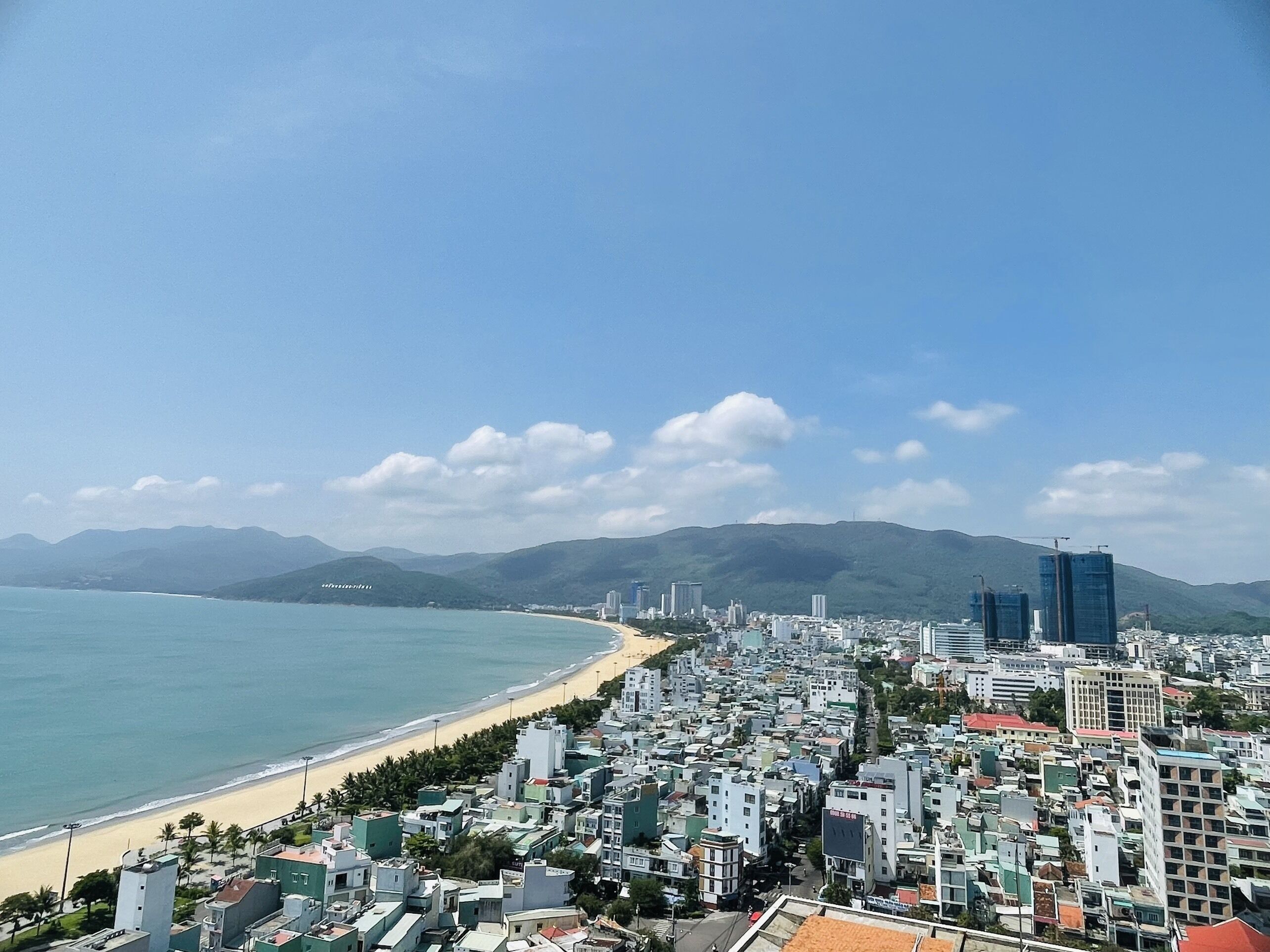 A coastal cityscape with a beach, buildings, and mountains in the background.
