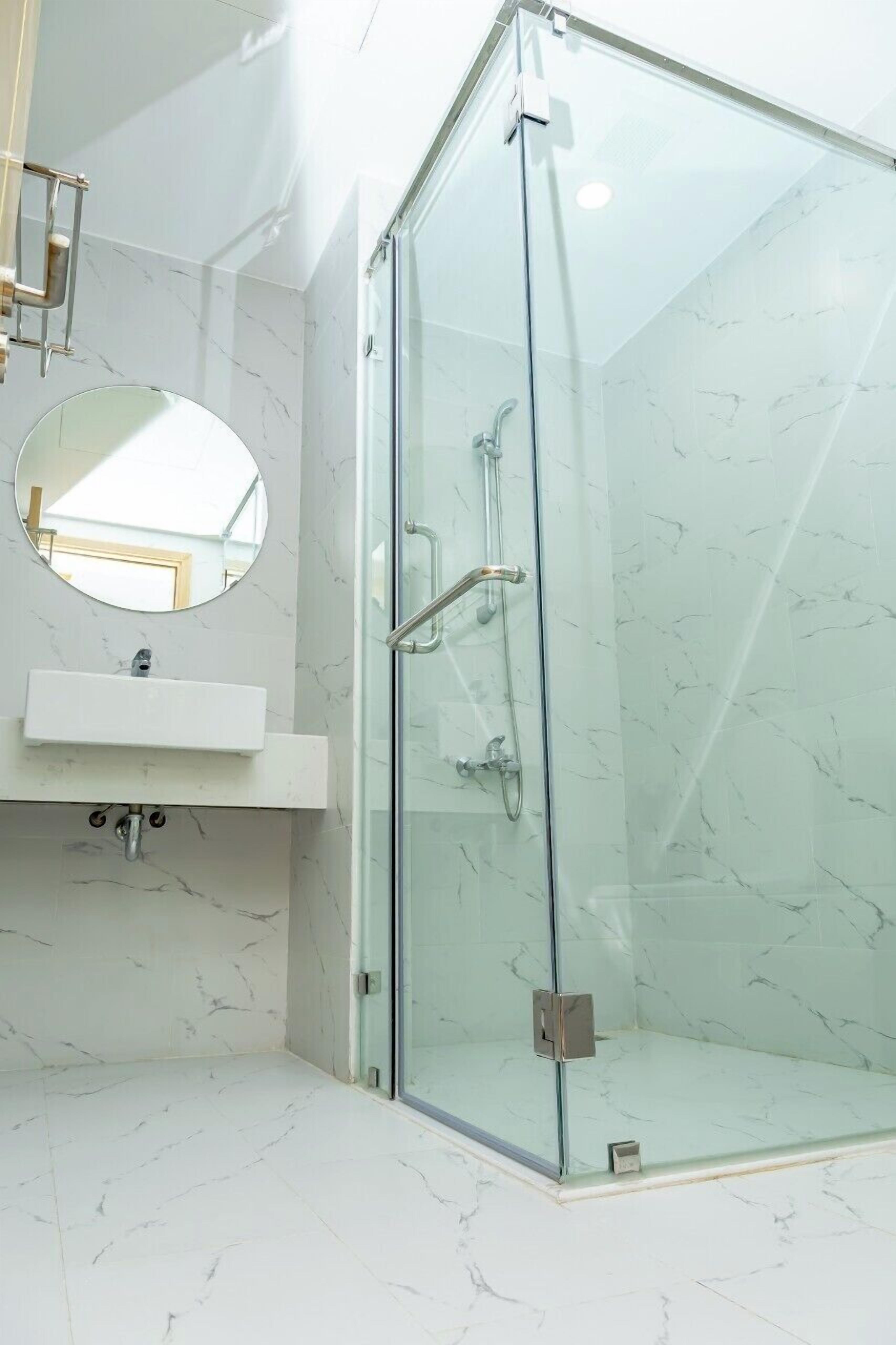 Une salle de bain moderne avec une douche à parois de verre, un miroir rond et un sol carrelé en marbre blanc.