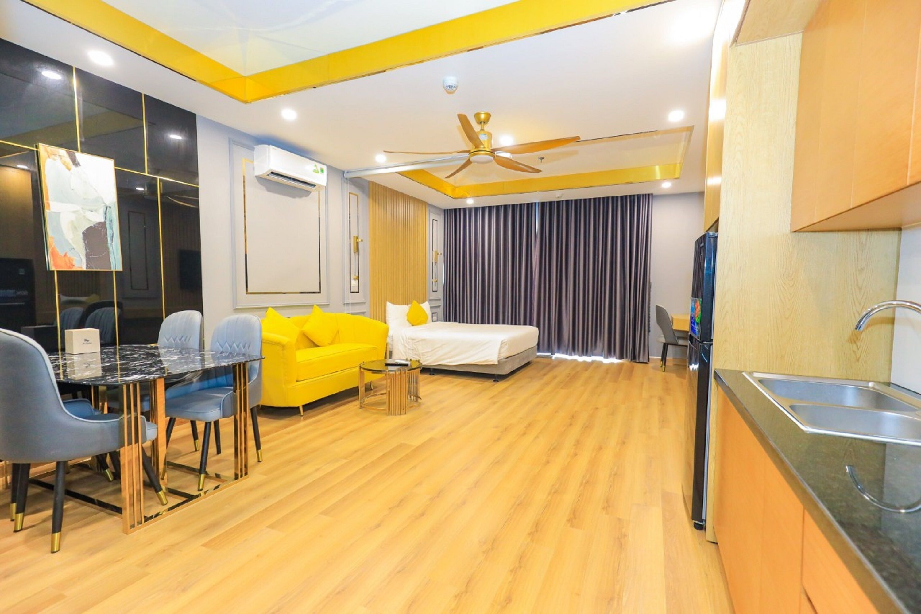 A modern hotel room with a dining area, a bed, a ceiling fan, and a kitchen area.