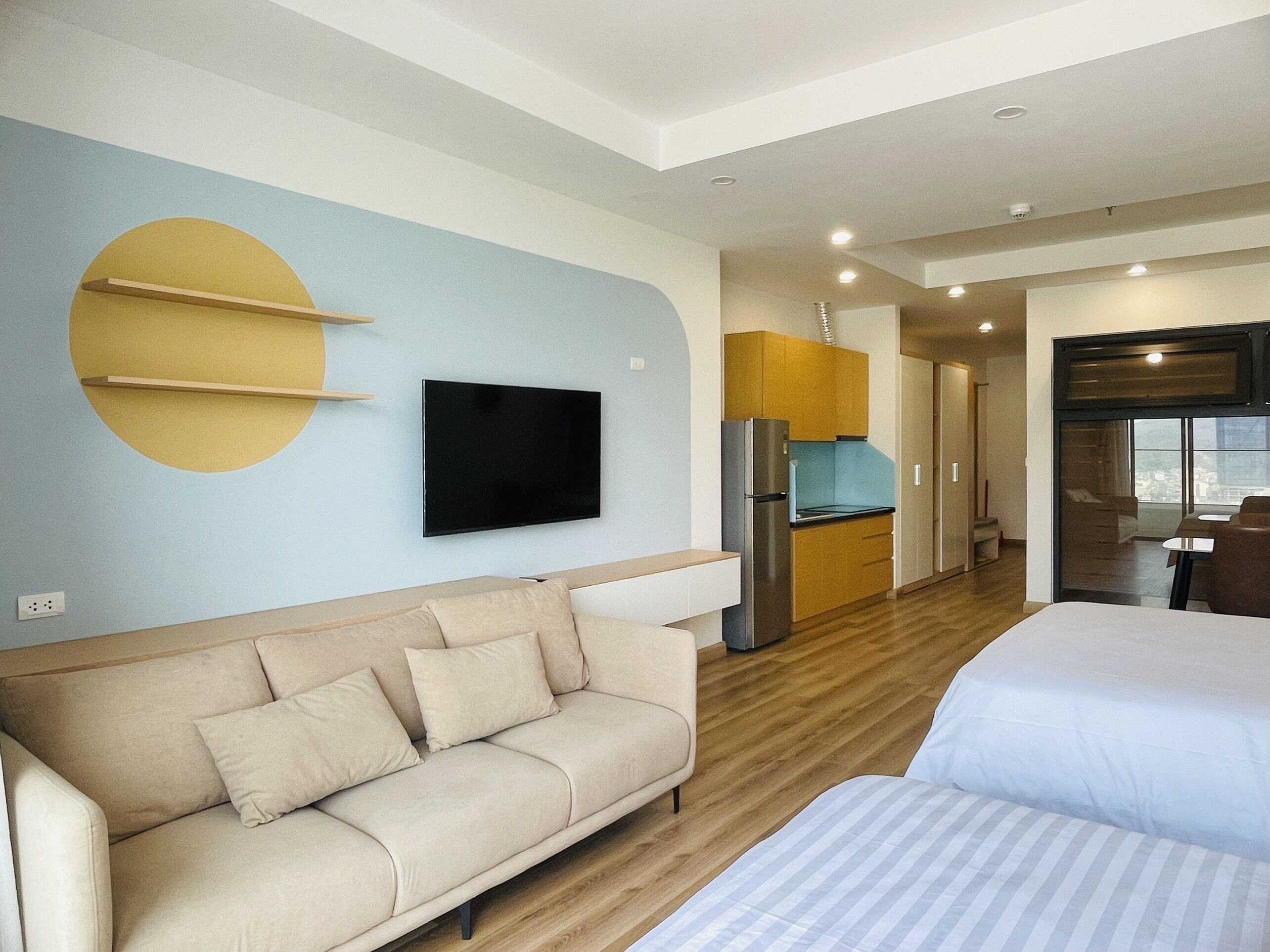 Un hotel moderno con sofá, cama, televisión montada en la pared, zona de cocina y vistas a la ciudad a través de la ventana.