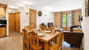 A dining area with wooden furniture, a kitchen with wooden cabinets, and a view of greenery through the window. - V Balme 02: Beside Ski Lift; Pool, Sauna & Gym, Vallorcine (Argentiere), France (Vallorcine (Argentiere))