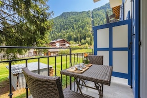 Un balcon agrémenté de meubles en osier, une table avec un plateau, et une vue sur une montagne et des bâtiments.