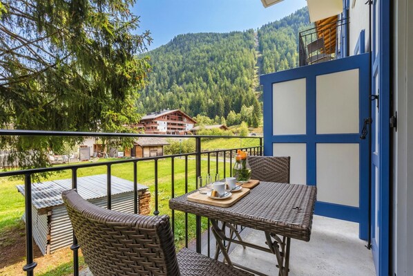 Een balkon met rieten meubels, een tafel met dienblad en uitzicht op een berg en gebouwen.