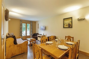 A dining area with a wooden table set for four, a sofa, and a television on the wall.