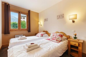 Une chambre d’hôtel avec deux lits, une fenêtre avec des rideaux, une lampe fixée au mur et une table de chevet avec un vase.