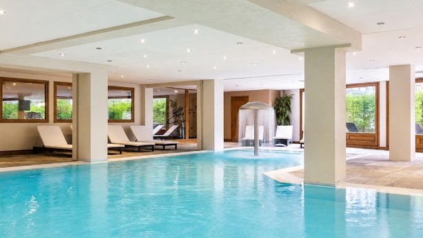 Une piscine intérieure dotée de chaises longues, d’un élément décoratif aquatique et de grandes fenêtres.