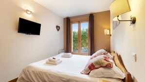Une chambre à coucher comprenant un lit, un téléviseur à écran plat, une fenêtre avec des rideaux et une lampe fixée au mur.