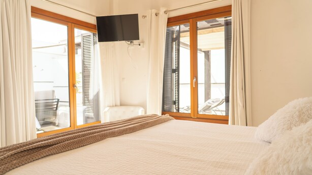 Een slaapkamer met een bed, een televisie en grote ramen.