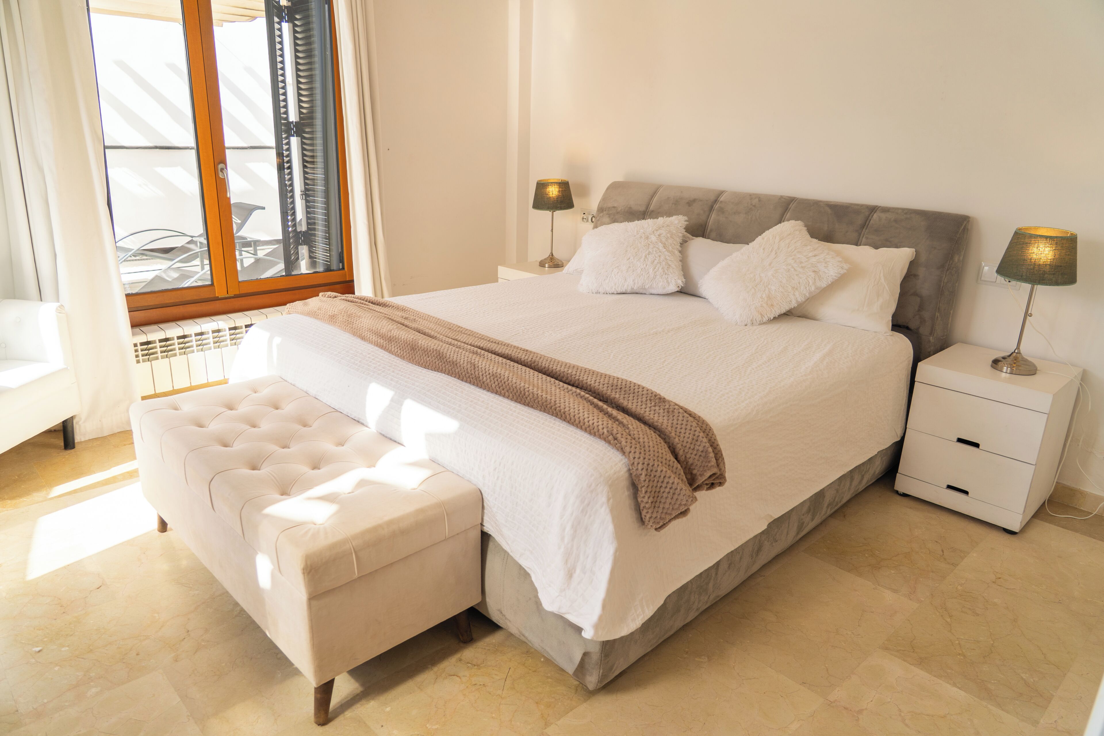 A bedroom with a large bed, a bedside table, a lamp, and a window with blinds.
