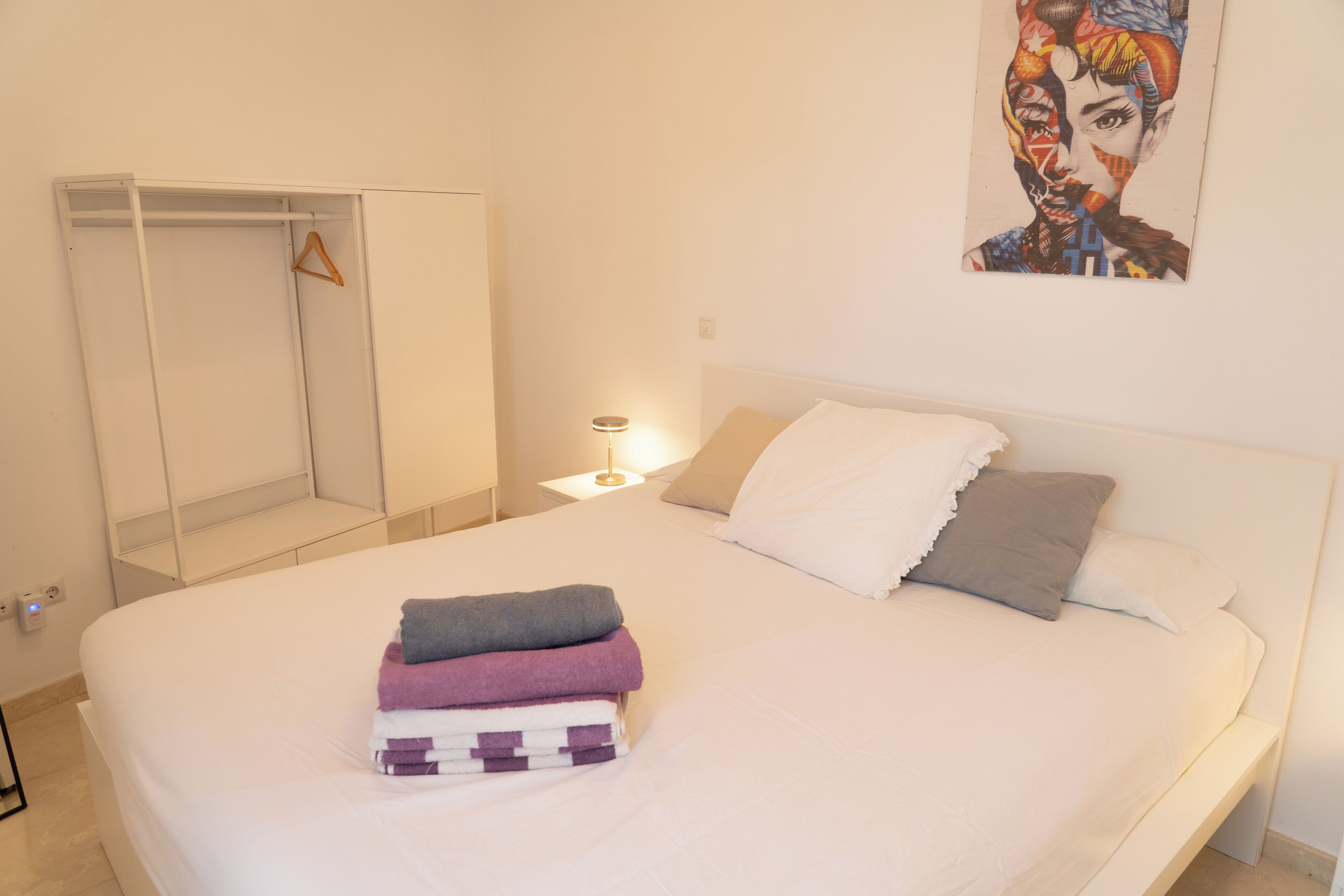 Une chambre à coucher avec un lit, une table de chevet avec une lampe, une armoire et un tableau au mur.