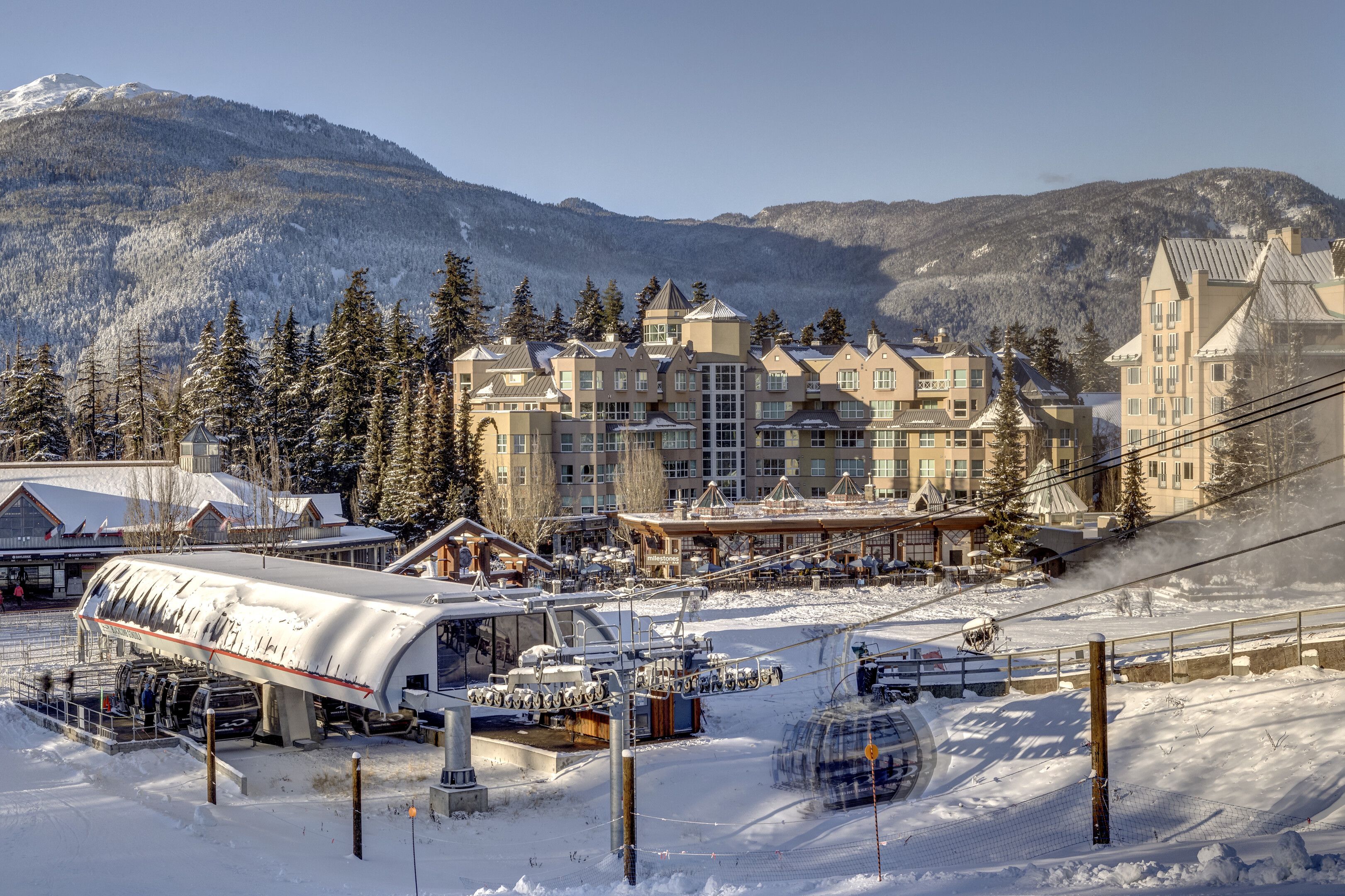 Une station de ski dotée d’un grand bâtiment, de remontées mécaniques et d’arbres couverts de neige.