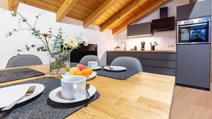 Uma cozinha moderna com teto de madeira, forno embutido e área de jantar com mesa posta para dois.
