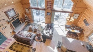 Et hyggeligt sommerhusinteriør med pejs, sofa, spisebord og store vinduer med udsigt til det sneklædte landskab.