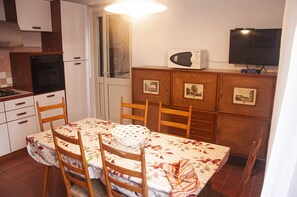 A compact kitchen with a dining table, chairs, a microwave, and a television.