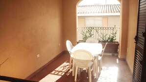 A balcony with a table and chairs, a view of a building with a tiled roof, and a metal railing.