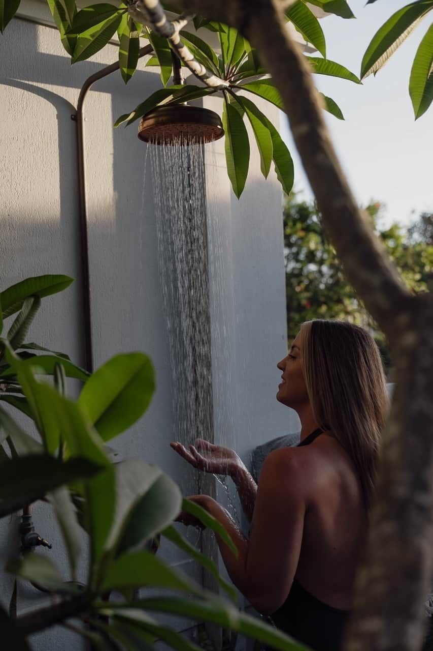 Eine Person steht unter einer Wasserfallbrause, im Vordergrund ein Baum.