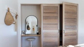 A bedroom with a bed, a wooden wardrobe, a mirror, a hanging bag, and a stool. - Sea Notes Beach House Yamba (Yamba)