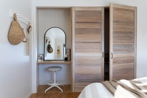 Une chambre à coucher avec un lit, une armoire en bois, un miroir, un sac suspendu et un tabouret.