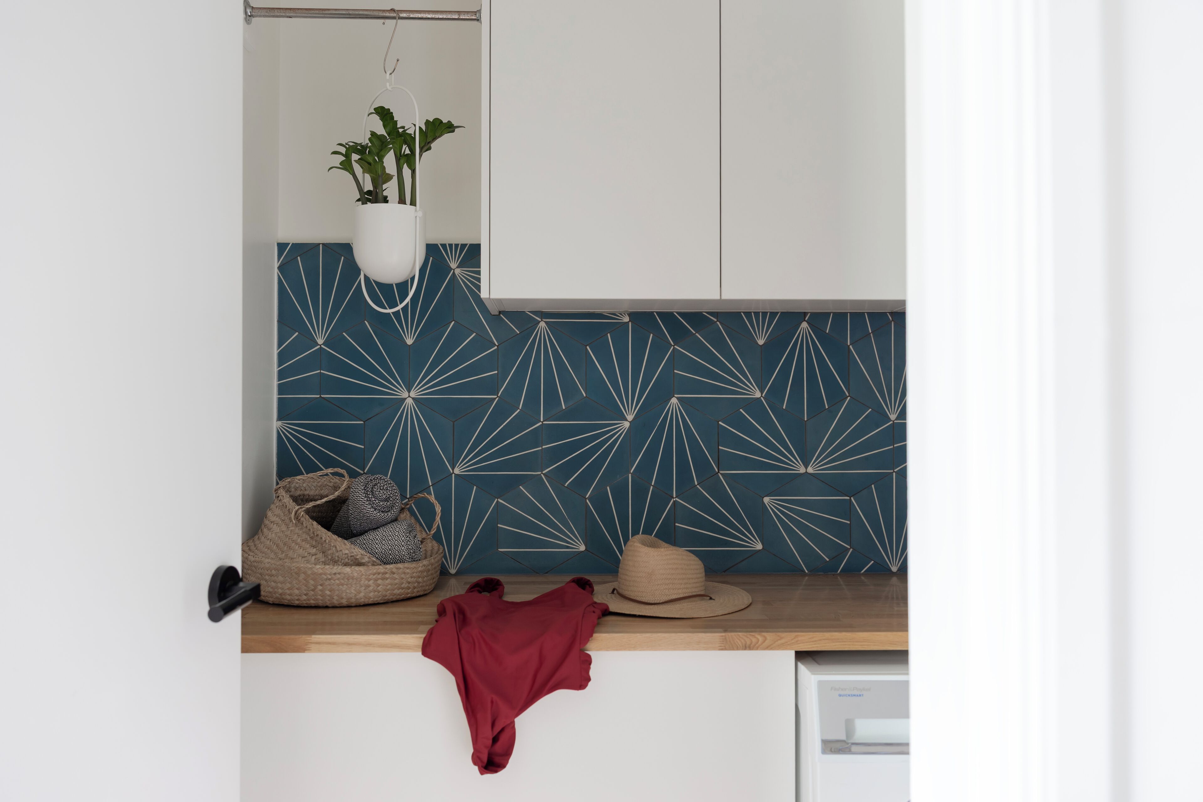 Een keuken met een blauwe geometrische spatwand, een hangplant, een geweven mand, een hoed en een rode doek op het aanrecht.