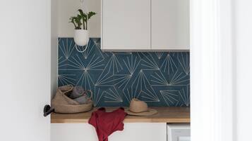 Een keuken met een blauwe geometrische spatwand, een hangplant, een geweven mand, een hoed en een rode doek op het aanrecht.