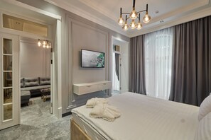 A modern hotel room with a large bed, a TV mounted on the wall, a seating area with a sofa, and a walk-in closet. - Continental Hotel (Samarkand)