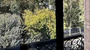 A balcony with a wrought iron railing, a clear view of trees and a road in the background. - Continental Hotel (Samarkand)