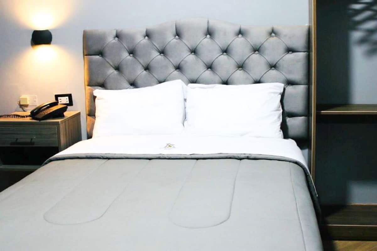 A neatly made bed with a tufted headboard, a bedside table with a lamp, and a small nightstand with a telephone.
